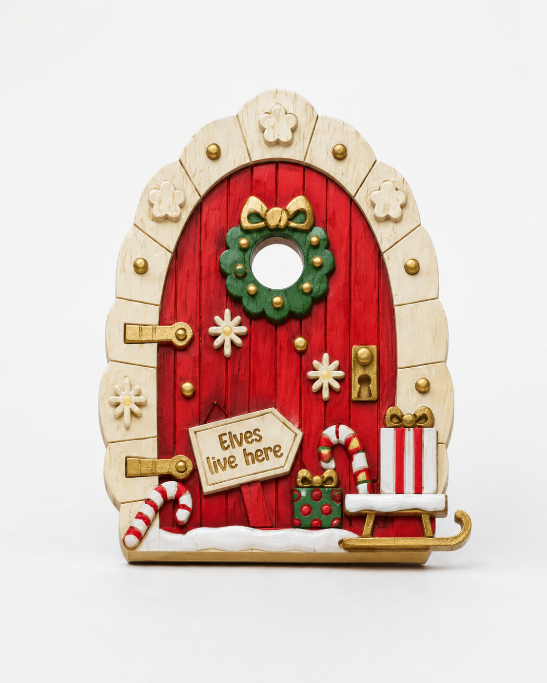 A decorative Christmas fairy door ornament with a red wooden-textured door, beige arched frame, green wreath, gold accents, candy canes, snow, and a sign reading 'Elves live here,' shown on a white background.
